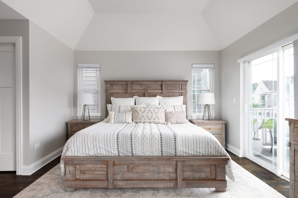 A beautiful bedroom with natural wood furniture, a glass door leading to a outdoor patio, and a cathedral ceiling.