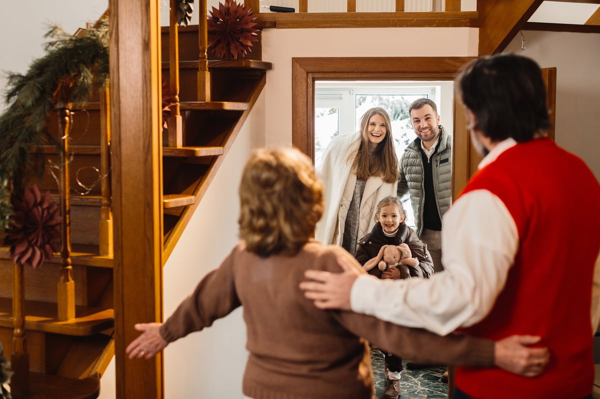 Grandparents greeting smiling family with young child arriving at decorated home for a joyful festive season celebration