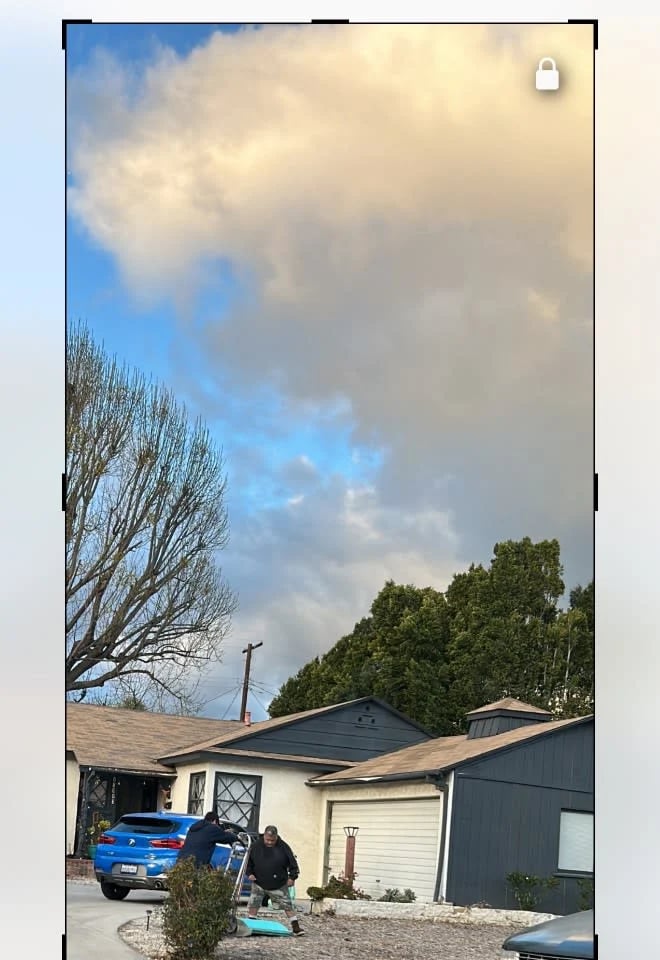 Single-story house with blue car parked in driveway, surrounded by trees against a cloudy sky