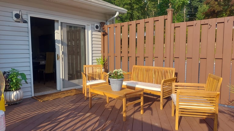 Wooden deck with yellow furniture and planters, brown fence, and house with open patio doors in background