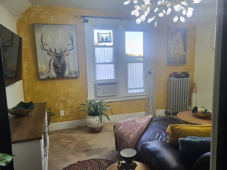 Cozy bedroom with yellow ochre walls, modern branched ceiling light, bed with burgundy bedding, leather seating, and deer artwork above a potted plant