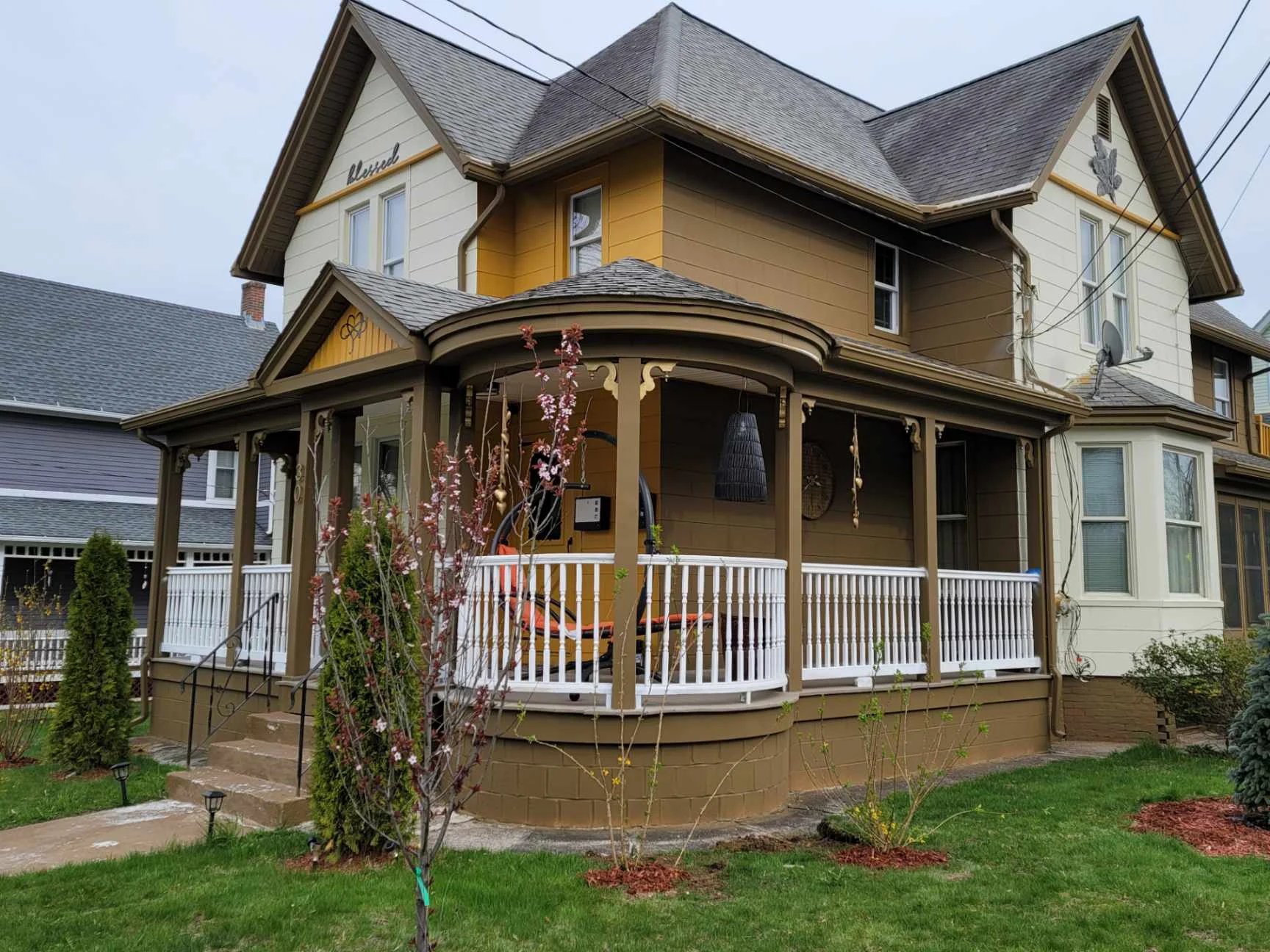 Victorian-style house with yellow and cream exterior, wrap-around porch, white railings, and gabled roof with ivy-covered columns
