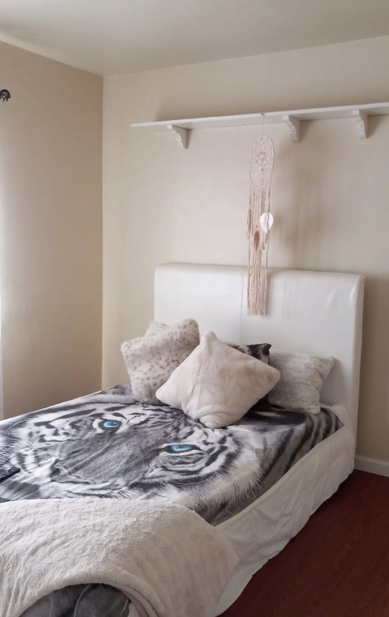 Minimalist bedroom with white bed, patterned bedding, decorative pillows, and macrame wall hanging above headboard