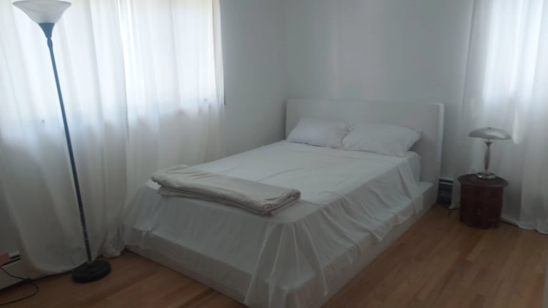 Minimalist bedroom with white bed, sheer curtains, floor lamp, and wooden flooring