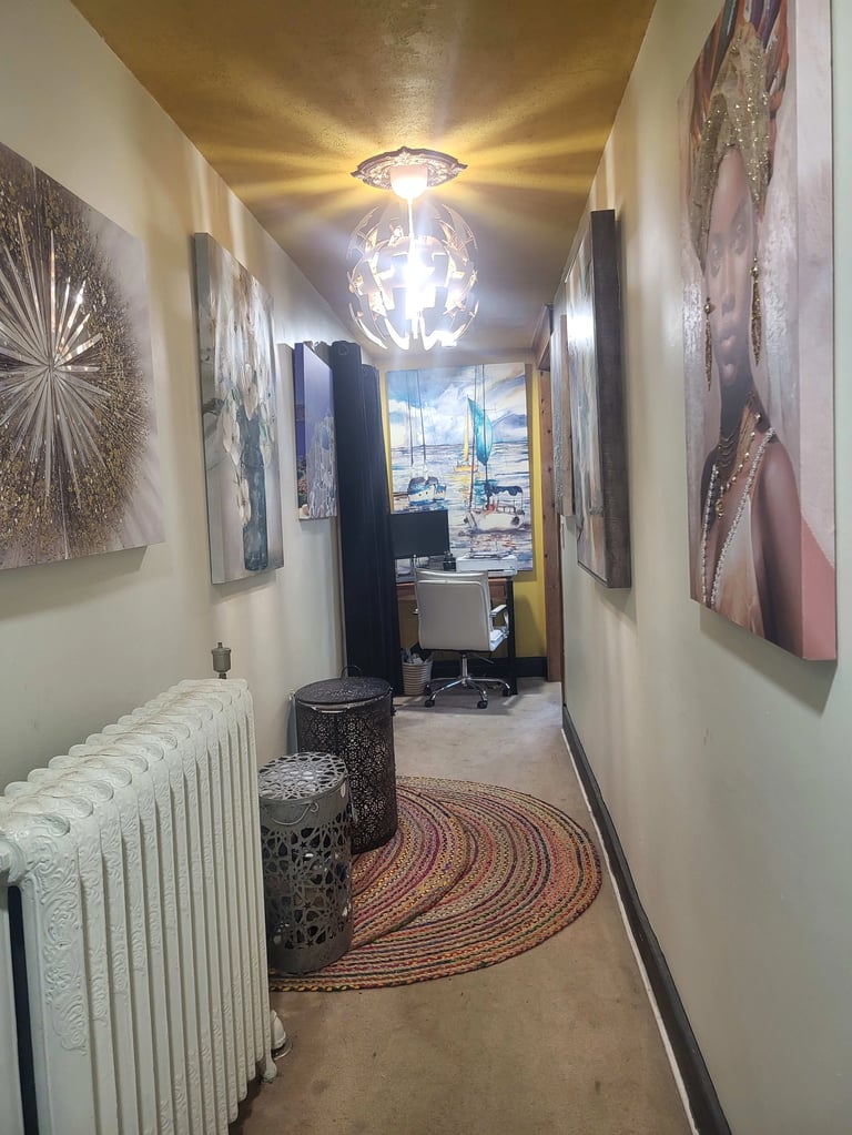 Modern hallway with decorative artwork, pendant light fixture, white radiator, patterned rug, and view of office workspace at end